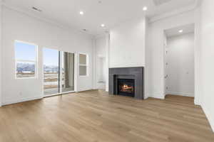 Unfurnished living room featuring a glass covered fireplace, light wood-type flooring, recessed lighting, a towering ceiling, and a mountain view