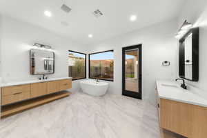Full bathroom with two vanities, a freestanding tub, and recessed lighting