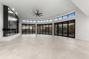 Unfurnished living room with a glass covered fireplace, a high ceiling, built in features, ceiling fan, and recessed lighting