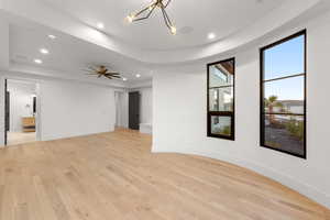 Spare room featuring light wood-style flooring, a raised ceiling, recessed lighting, and a chandelier