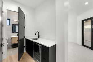 Bar featuring dark cabinetry, modern cabinets, beverage cooler, light stone counters, and recessed lighting