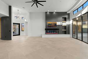 Unfurnished living room featuring a towering ceiling, a chandelier, recessed lighting, a ceiling fan, and a glass covered fireplace