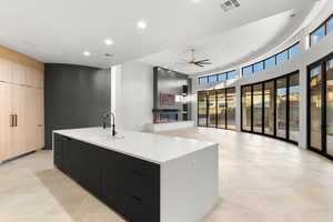 Kitchen featuring modern cabinets, an island with sink, recessed lighting, ceiling fan, and a towering ceiling