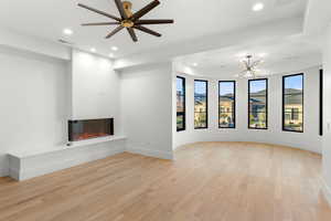 Unfurnished living room with a glass covered fireplace, light wood-type flooring, recessed lighting, a chandelier, and a ceiling fan