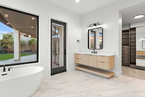 Full bathroom with vanity, a walk in closet, a freestanding bath, light marble finish flooring, and recessed lighting