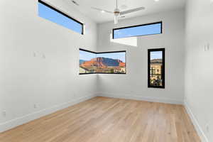 Spare room with light wood-type flooring, healthy amount of natural light, a high ceiling, and ceiling fan
