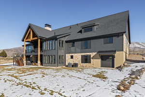 Snow covered back of property featuring stone siding, a mountain view, a patio, and a balcony