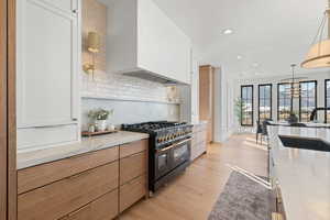 Kitchen featuring range with two ovens, premium range hood, light stone counters, tasteful backsplash, and recessed lighting