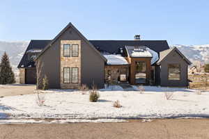 View of front of property featuring a mountain view, stone siding, a garage, a chimney, and driveway