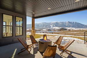 Snow covered back of property with a mountain view, a patio, and an outdoor fire pit