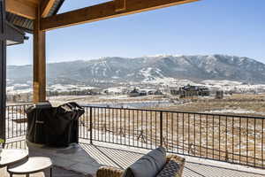 Snow covered back of property featuring grilling area, a mountain view, and a patio