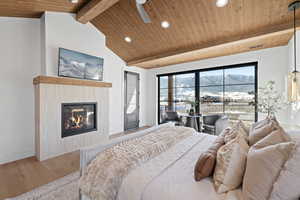 Bedroom with access to outside, a glass covered fireplace, wooden ceiling, wood finished floors, and recessed lighting