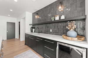 Bar with open shelves, dark cabinetry, wine cooler, light wood-type flooring, and tasteful backsplash