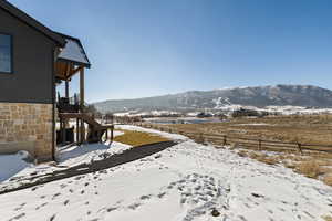 Yard covered in snow featuring a mountain view, stairway, and a patio