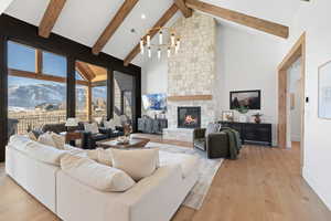 Living area with a mountain view, a stone fireplace, light wood-style floors, high vaulted ceiling, and a chandelier