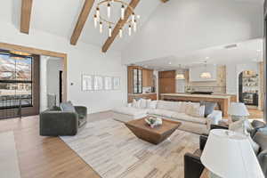 Living room featuring arched walkways, a chandelier, high vaulted ceiling, light wood-style floors, and beam ceiling