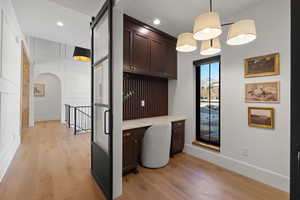 Bar featuring built in desk, dark brown cabinets, arched walkways, light wood-style flooring, and pendant lighting
