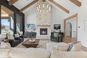 Living room with high vaulted ceiling, wood finished floors, a stone fireplace, beam ceiling, and arched walkways