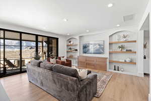 Living area with built in shelves, light wood finished floors, and recessed lighting