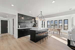 Indoor wet bar featuring dark cabinetry, pendant lighting, light countertops, open shelves, and light wood finished floors