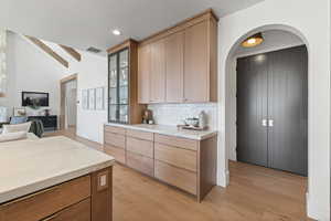 Kitchen with light brown cabinets, tasteful backsplash, light wood-type flooring, arched walkways, and modern cabinets