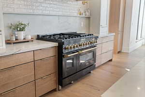 Kitchen featuring tasteful backsplash, double oven range, light stone counters, light wood-type flooring, and modern cabinets