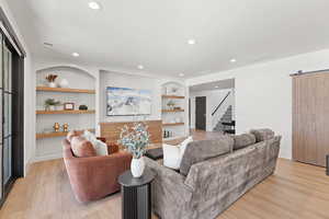 Living room with built in features, a barn door, light wood-type flooring, recessed lighting, and stairway