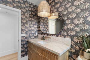 Bathroom with wallpapered walls, vanity, and light wood-style floors