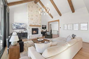 Living area featuring high vaulted ceiling, a stone fireplace, light wood-style floors, beam ceiling, and a chandelier