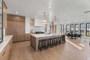 Kitchen featuring a kitchen bar, hanging light fixtures, a large island with sink, recessed lighting, and light wood-style flooring