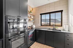 Kitchen with stainless steel double oven, dark cabinets, light floors, open shelves, and a mountain view