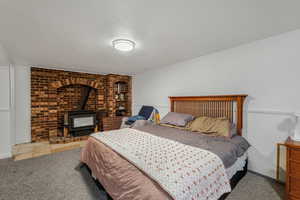 Bedroom featuring a wood stove, carpet floors, and a textured ceiling