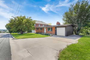 View of front of property featuring brick siding, a front yard, concrete driveway, a chimney, and a garage