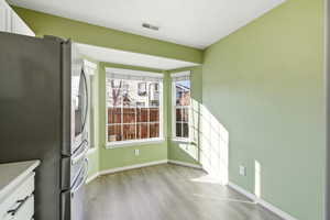 Kitchen with stainless steel fridge with ice dispenser, white cabinetry, light wood-type flooring, and light stone counters