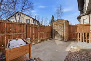 Fenced backyard featuring a gate, a storage shed, and a patio area