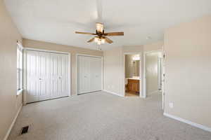 Unfurnished bedroom featuring multiple closets, light colored carpet, connected bathroom, and ceiling fan