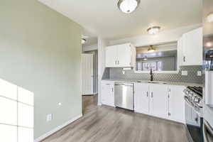 Kitchen with stainless steel appliances, white cabinetry, light wood-style flooring, light stone countertops, and tasteful backsplash