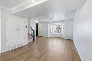 Unfurnished living room with ornamental molding, light wood-style flooring, and stairway