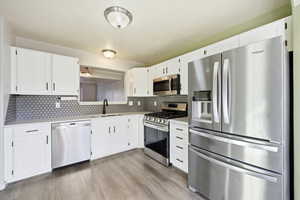 Kitchen featuring appliances with stainless steel finishes, white cabinets, light wood-style floors, backsplash, and light stone counters