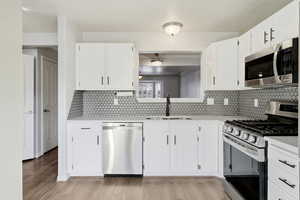 Kitchen with appliances with stainless steel finishes, white cabinets, light stone counters, and light wood finished floors