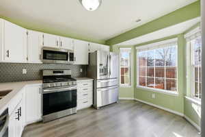 Kitchen with appliances with stainless steel finishes, white cabinetry, tasteful backsplash, and light stone counters