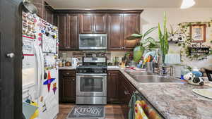 Kitchen with stainless steel appliances, dark brown cabinets, backsplash, and dark wood-style floors
