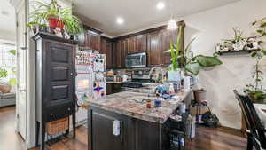 Kitchen featuring dark brown cabinets, appliances with stainless steel finishes, a peninsula, light countertops, and dark wood-style flooring
