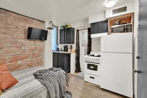 Kitchen with white appliances, light countertops, light wood-style flooring, dark cabinets, and under cabinet range hood