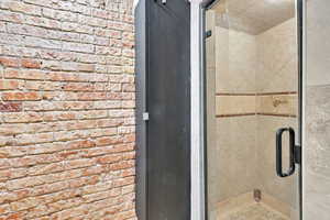 Bathroom featuring a shower stall and brick wall