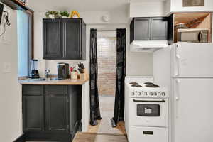 Kitchen featuring white appliances, light countertops, custom range hood, and light wood finished floors