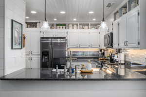 Kitchen with dark stone countertops, stainless steel appliances, decorative backsplash, white cabinetry, and recessed lighting
