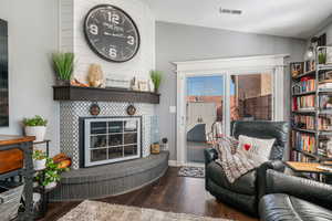 Living room featuring vaulted ceiling, a fireplace, and dark wood-type flooring