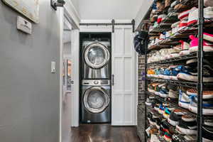 Laundry area featuring a barn door, dark wood finished floors, a textured wall, and stacked washer and clothes dryer