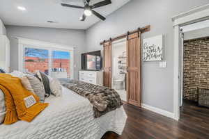 Bedroom featuring a barn door, access to outside, dark wood finished floors, ceiling fan, and connected bathroom